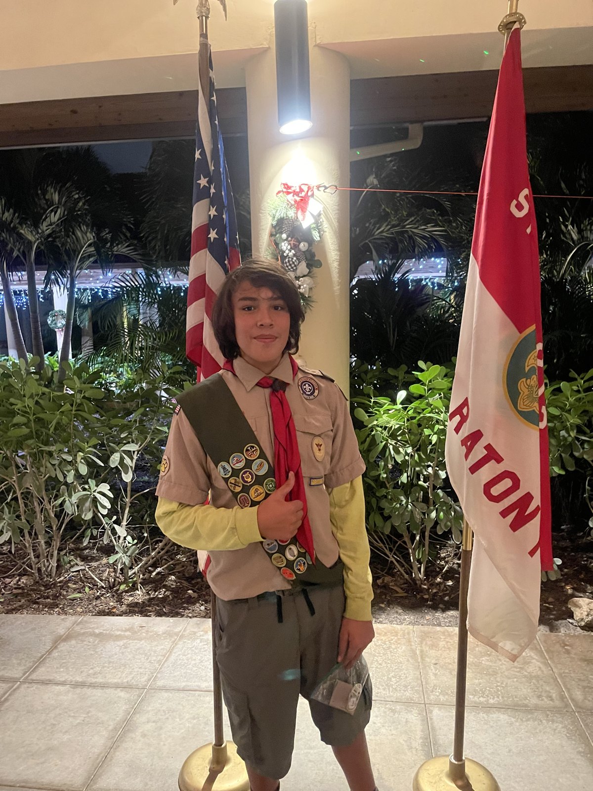 Jack wearing his merit badge sash beside the flags